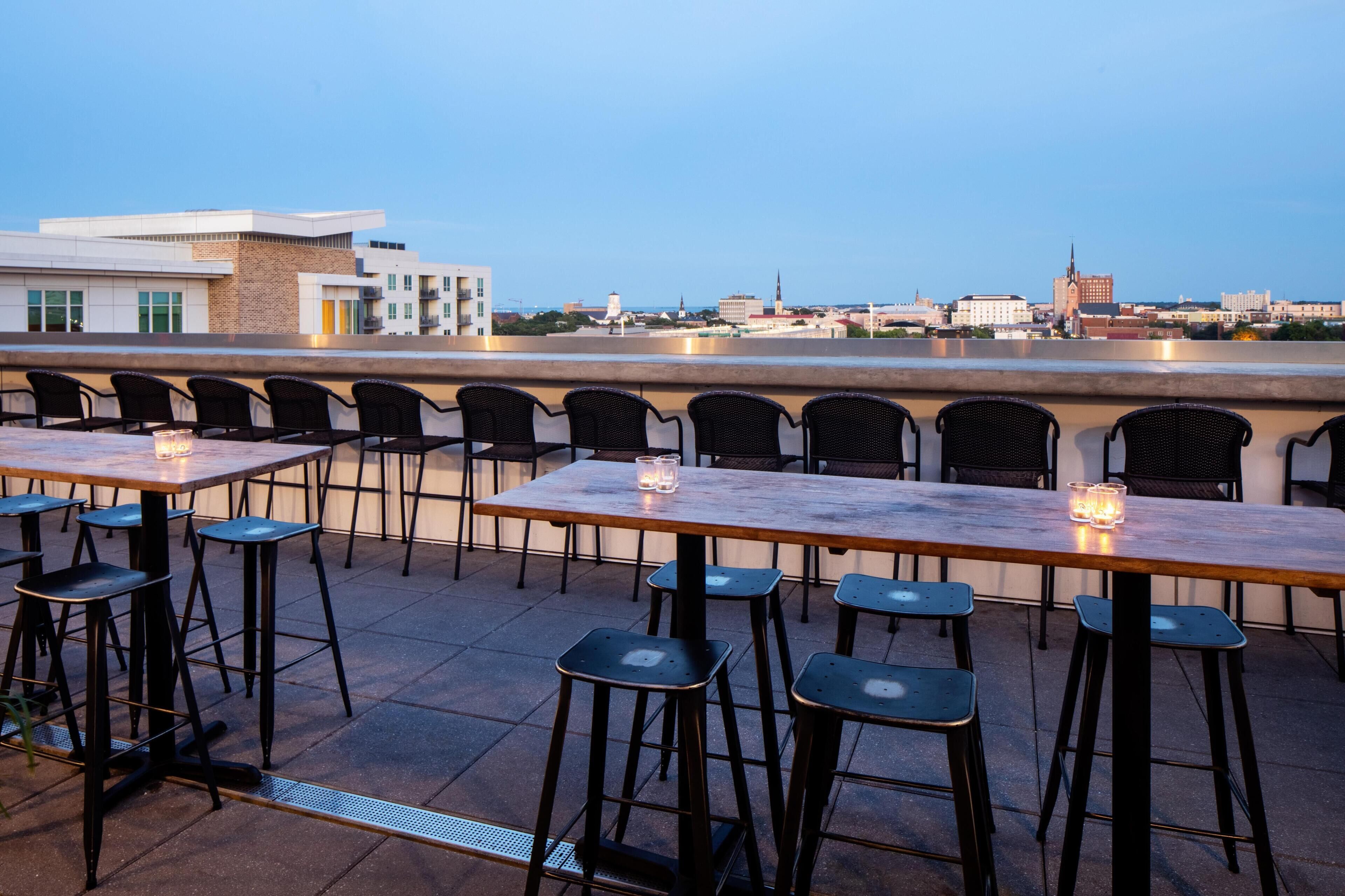 An outdoor dining area with tables and chairs, a view of the city skyline, and a building with a spire.