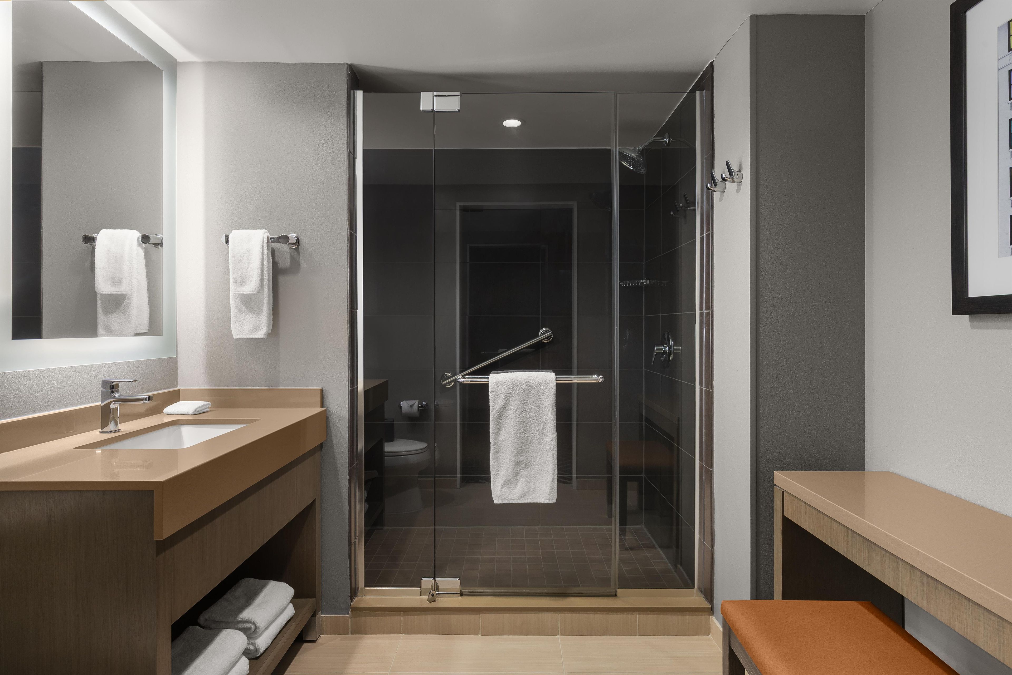 Une salle de bain moderne avec une douche à parois de verre, un lavabo et un banc.