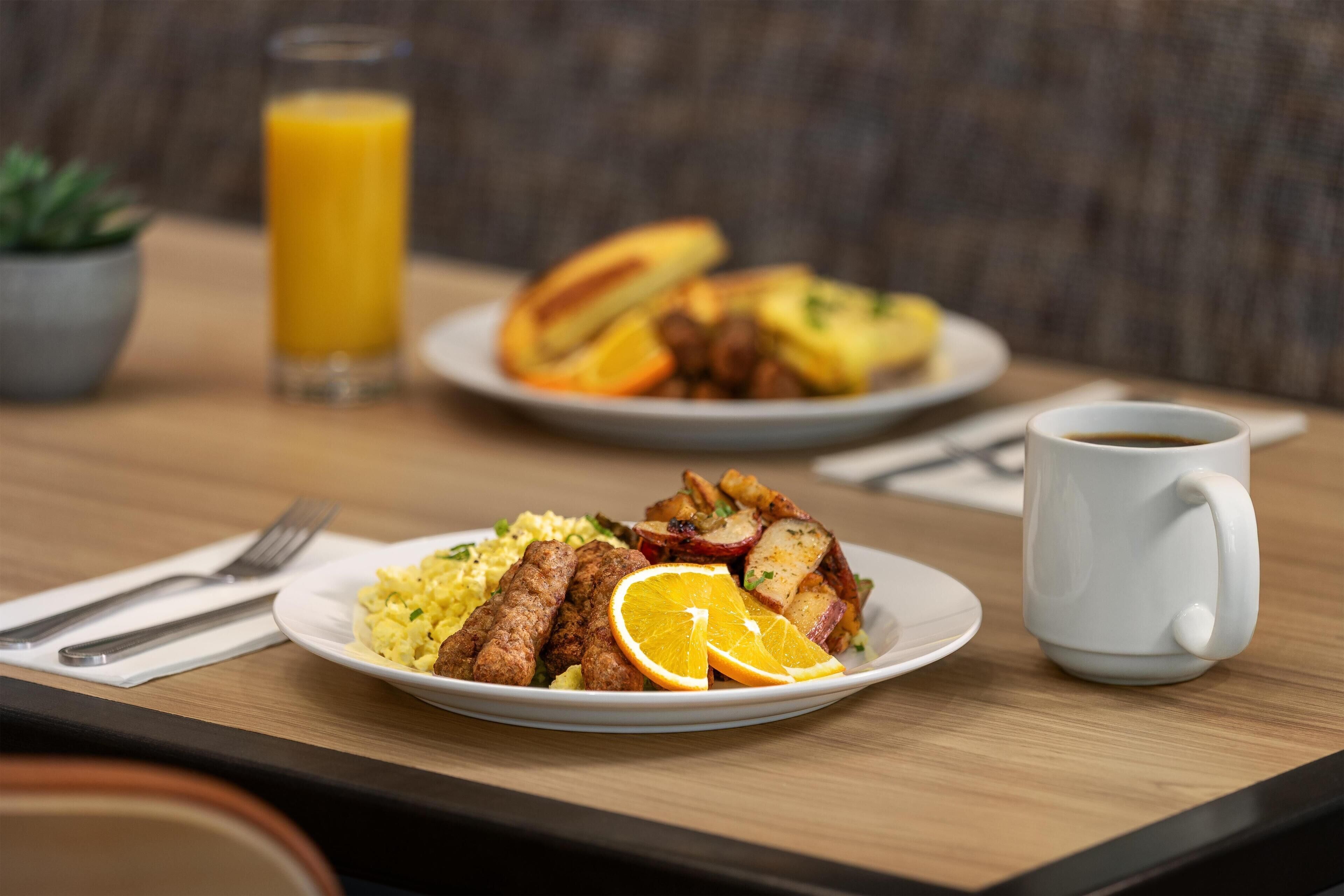 A breakfast setting with plates of food, a glass of orange juice, and a coffee mug on a wooden table.