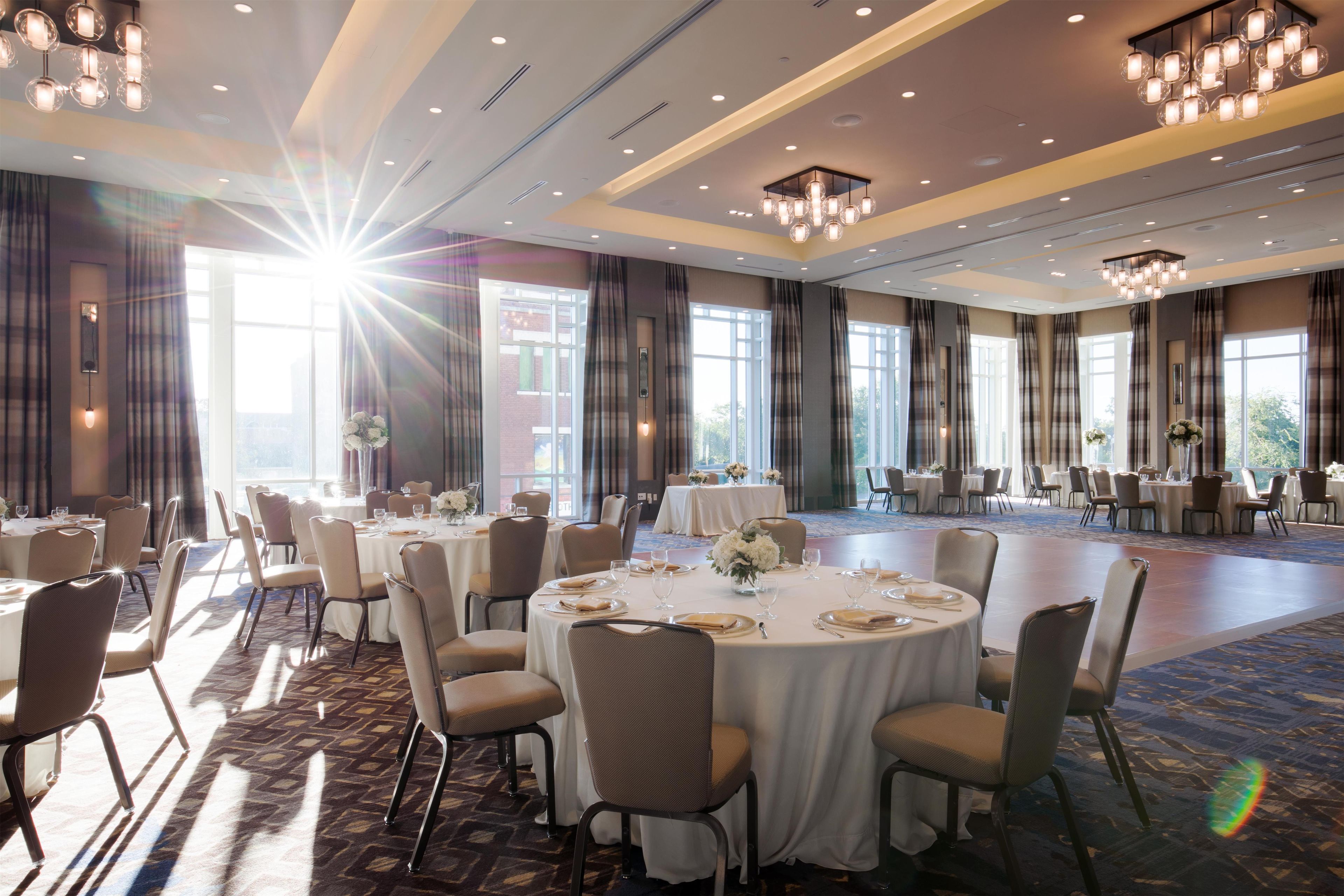 Un salón de banquetes con mesas redondas dispuestas para comer, ventanas amplias y candelabros.