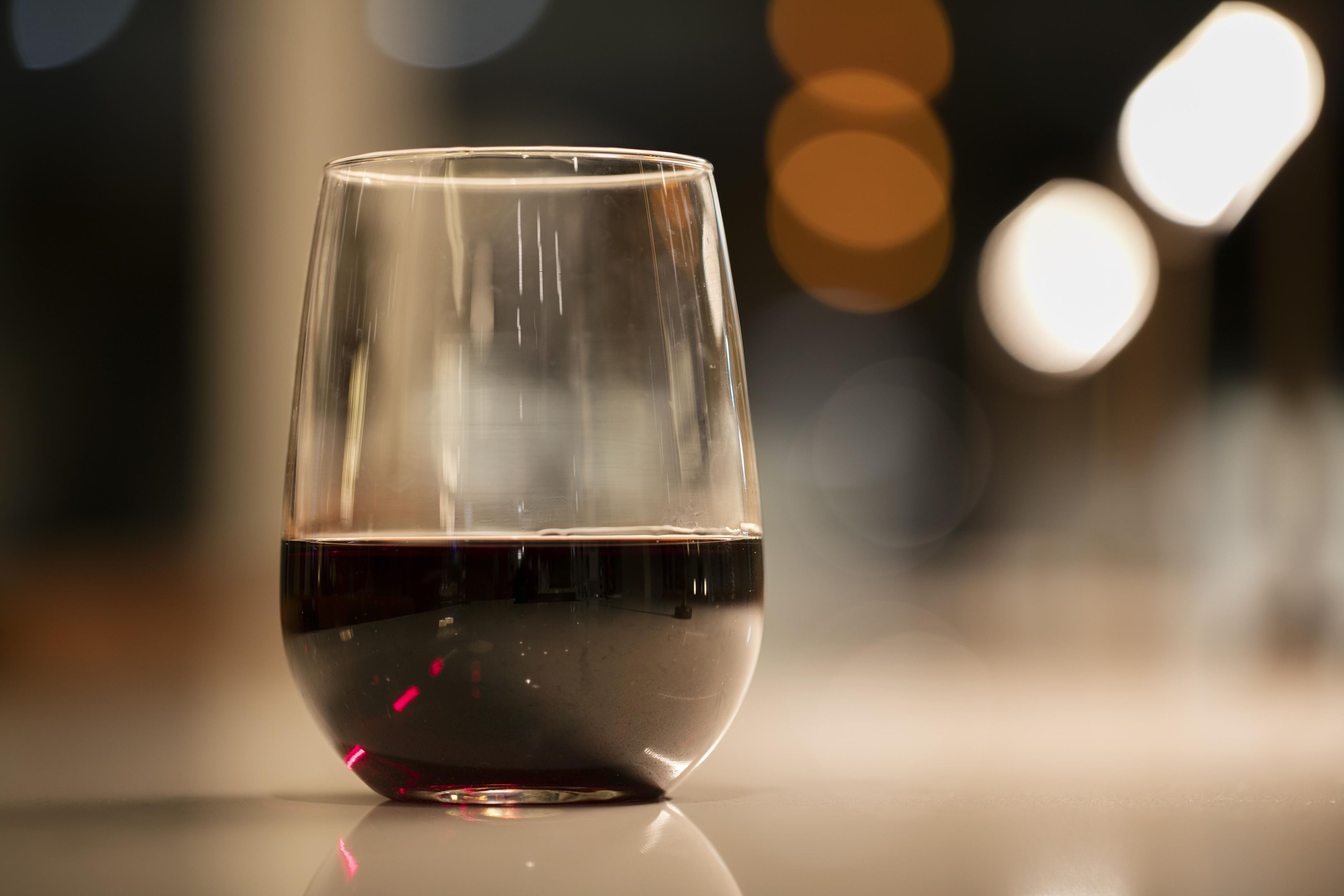 Ein klares Glas mit einer Flüssigkeit, möglicherweise Wein, auf einer spiegelnden Oberfläche.