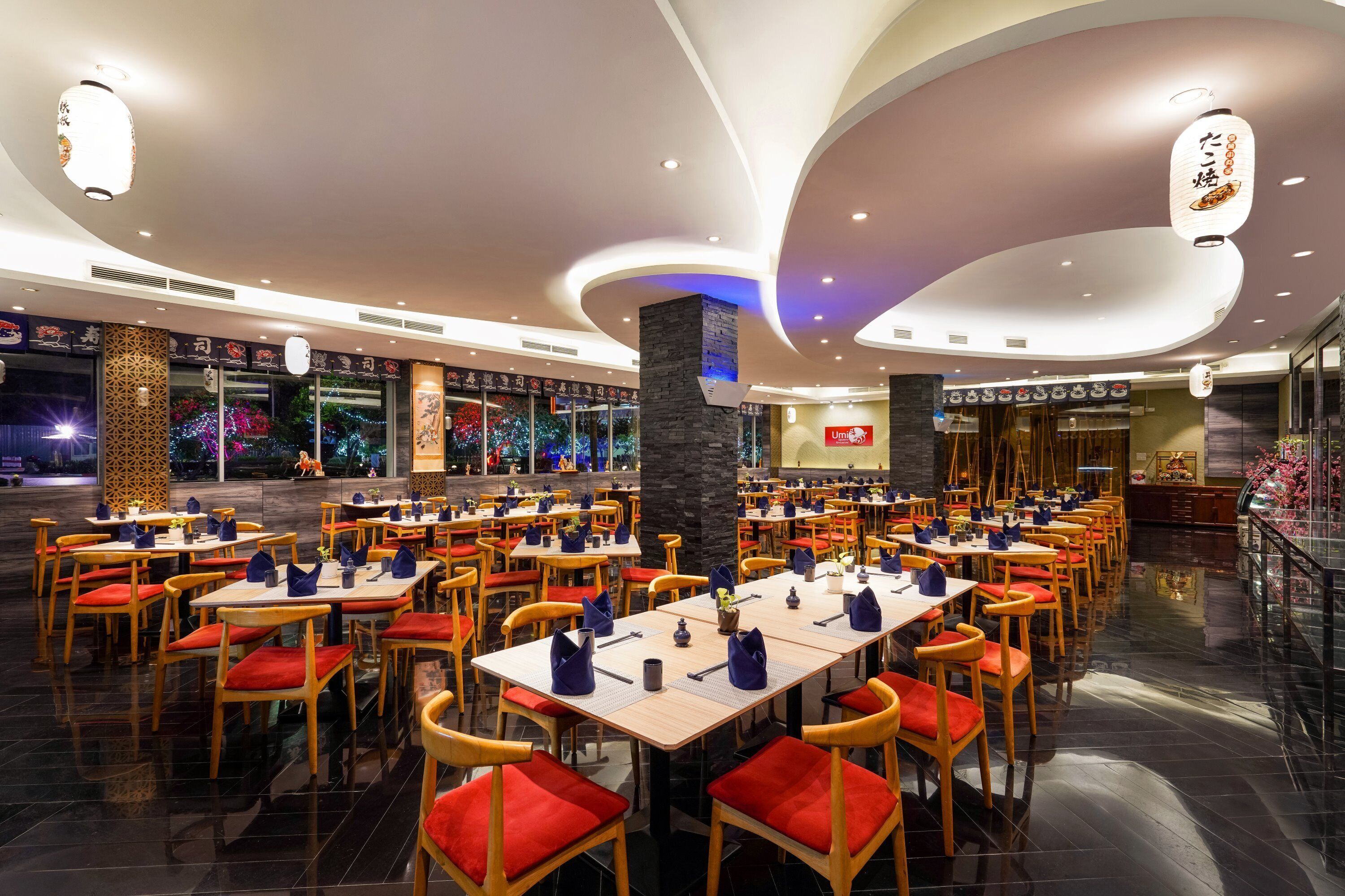 A spacious dining area with multiple tables and chairs, a central pillar, and a modern ceiling design.