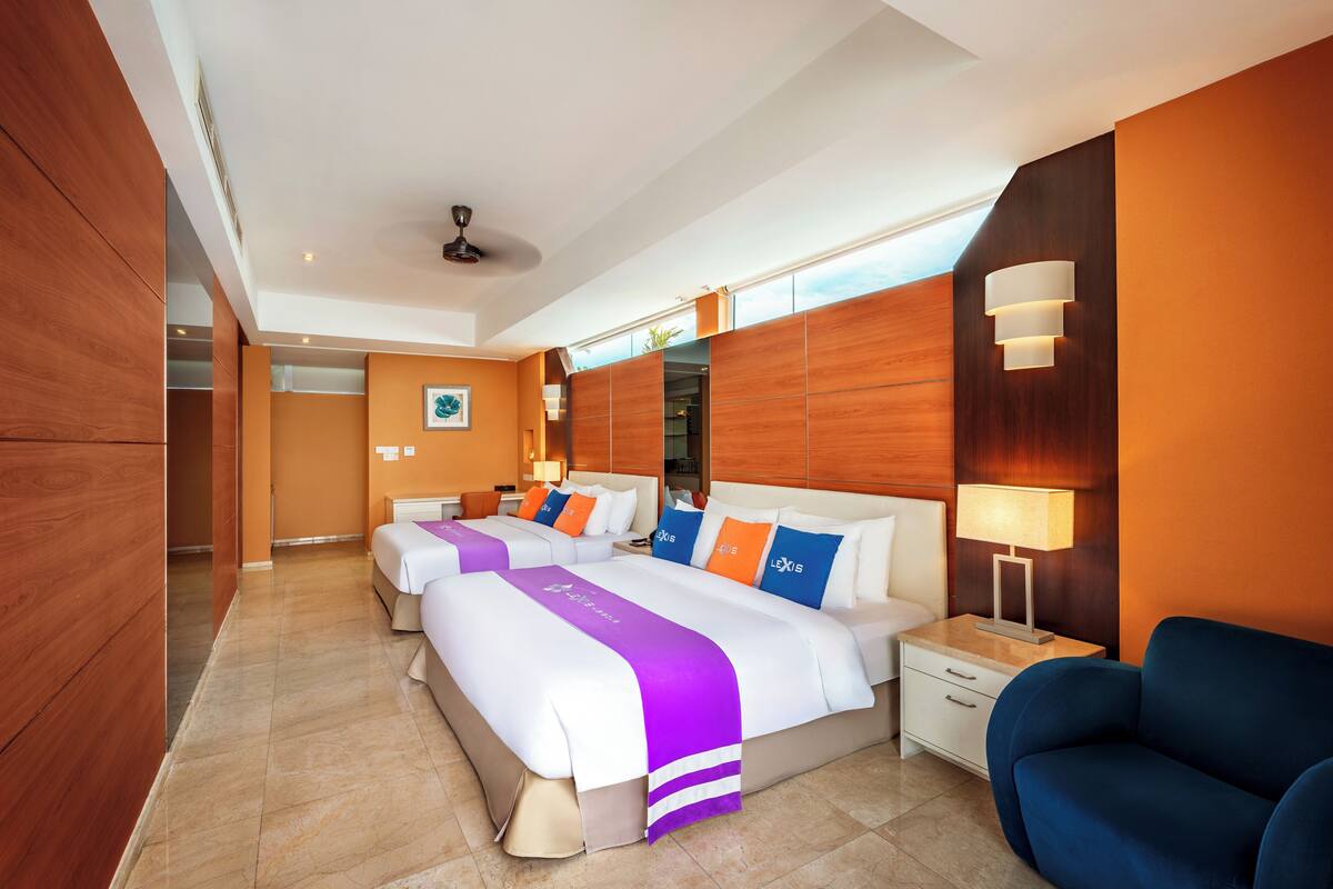 A hotel room with two beds, a blue armchair, a nightstand, and a ceiling fan.