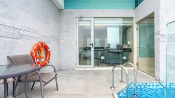 A pool area with a glass door leading to a room, a table with chairs, and an orange life ring on the wall.