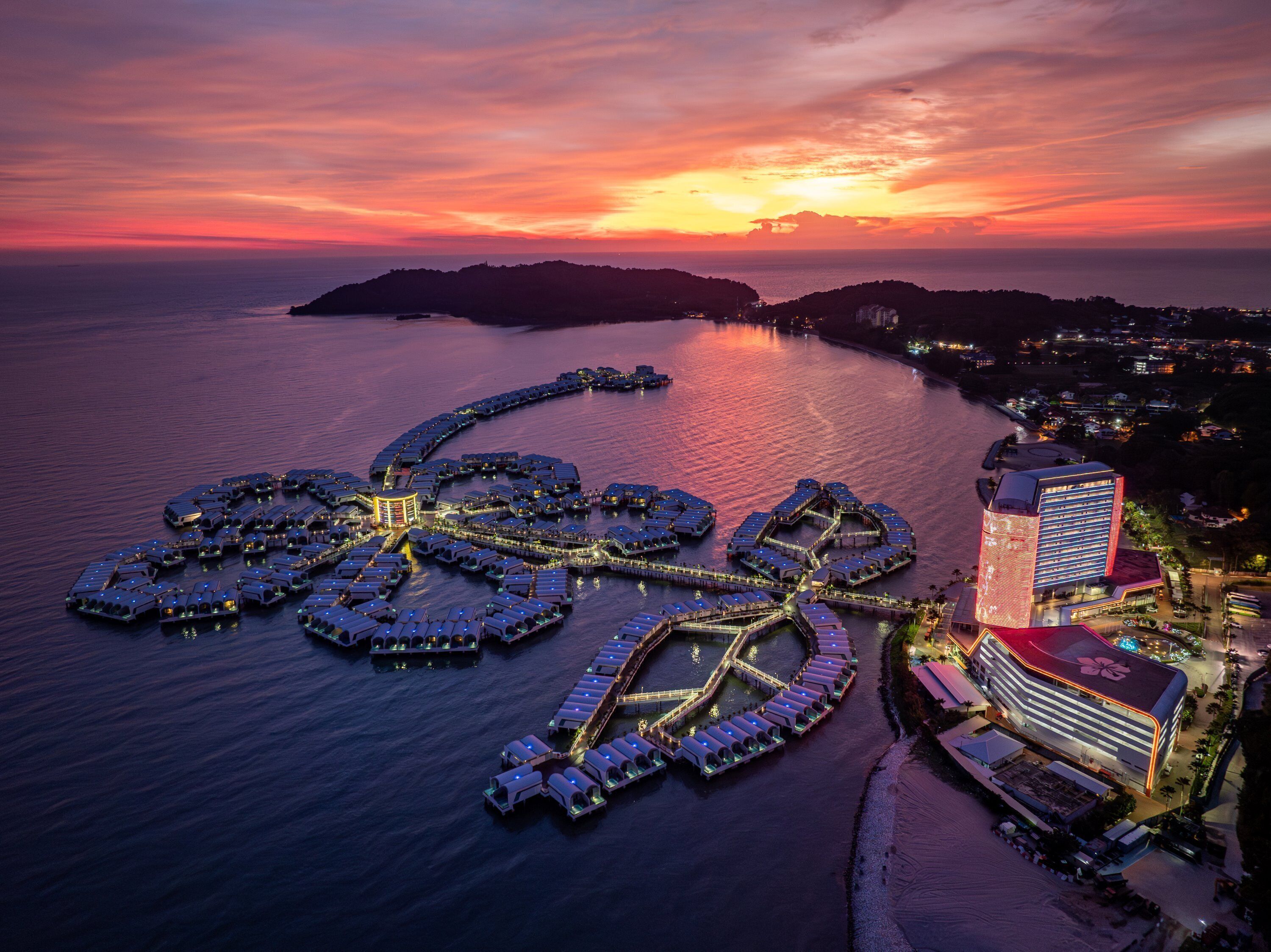 An aerial view of a waterfront resort with multiple docked boats, a central building, and a large hotel structure.