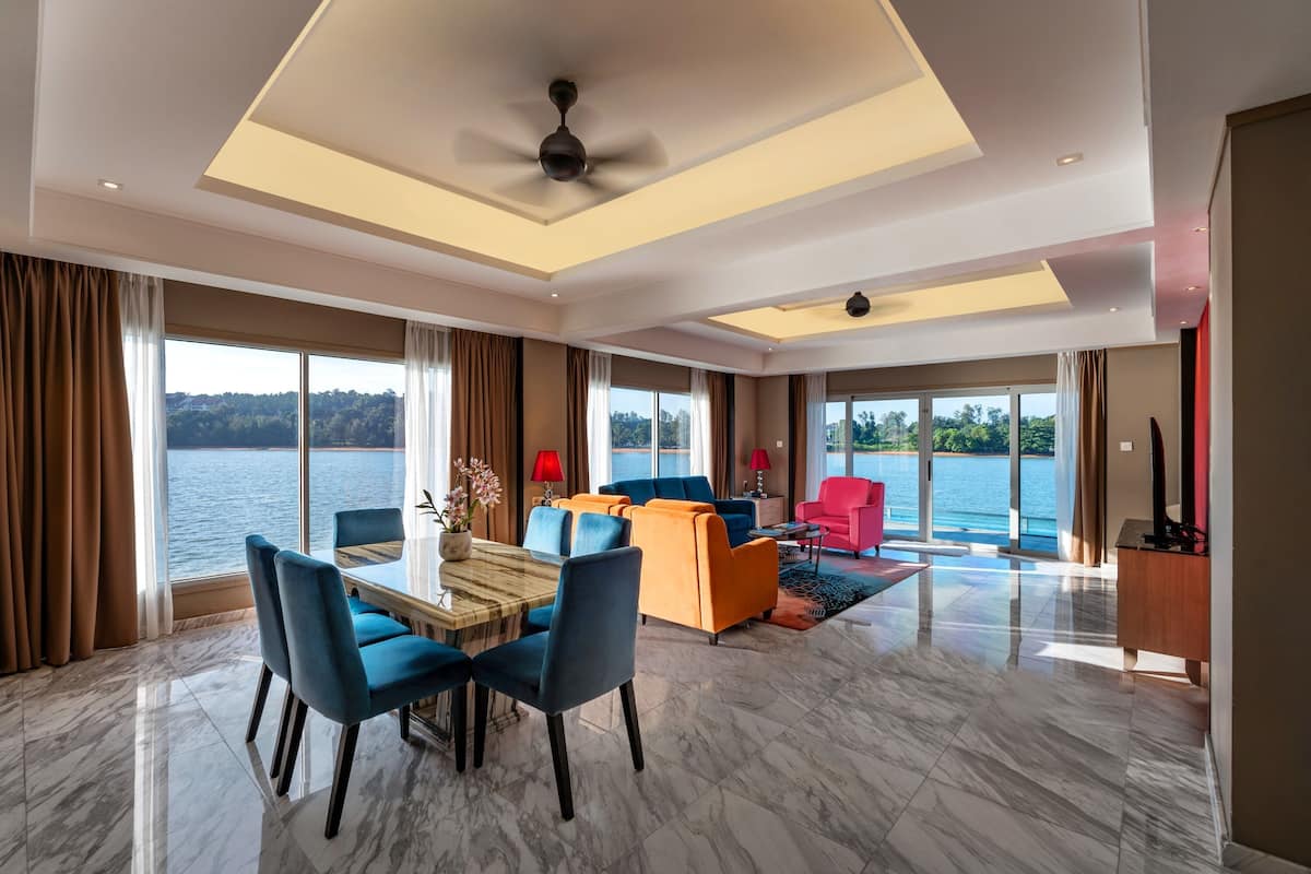 A spacious living area with a dining table, blue and orange sofas, a red armchair, and a view of the water.