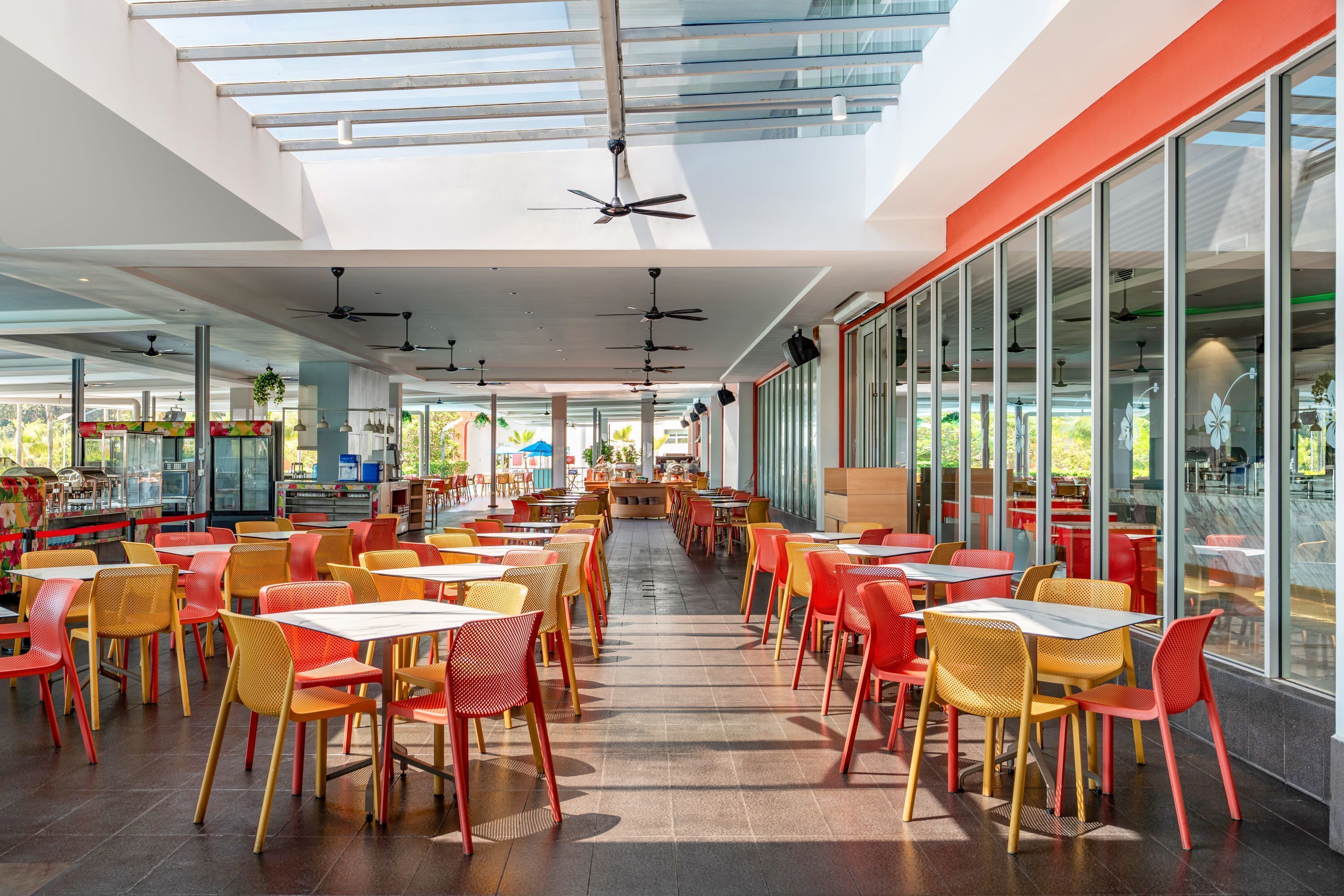 A spacious indoor area with multiple tables and chairs, large windows, and ceiling fans.