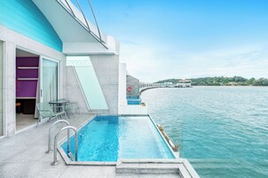 A modern pool area with a clear view of the water, a glass door leading to a room, and a chair by the pool.