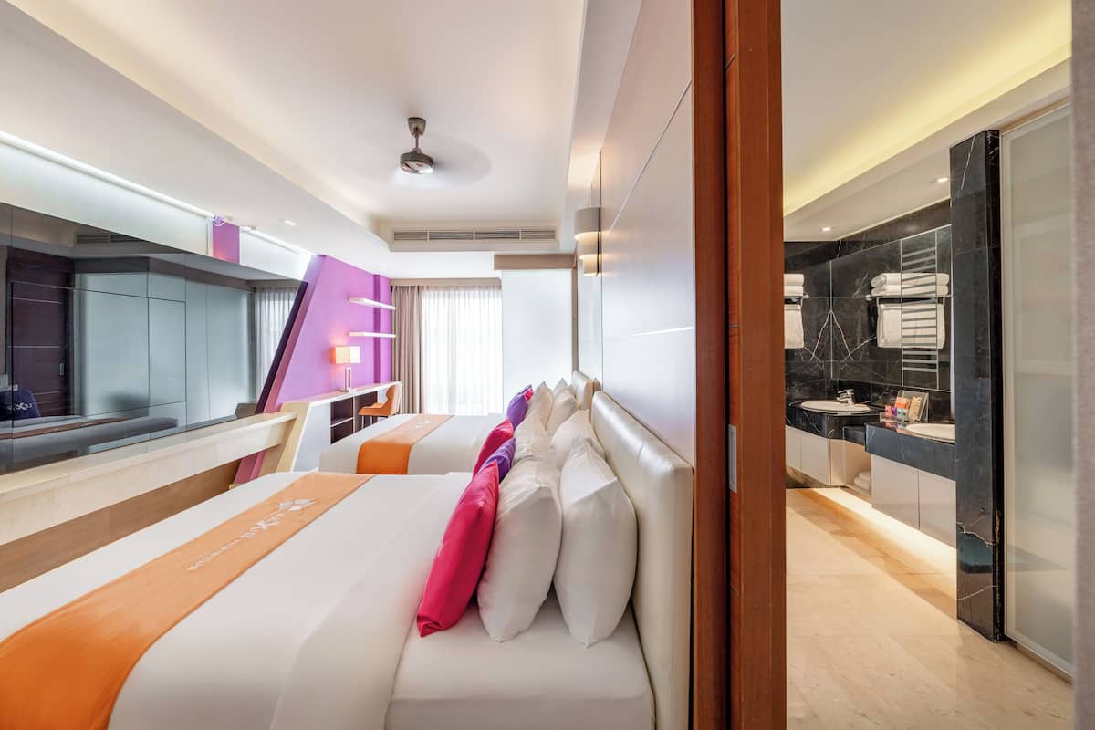 A modern hotel room with a large bed, a desk, and a bathroom with a vanity and mirror.