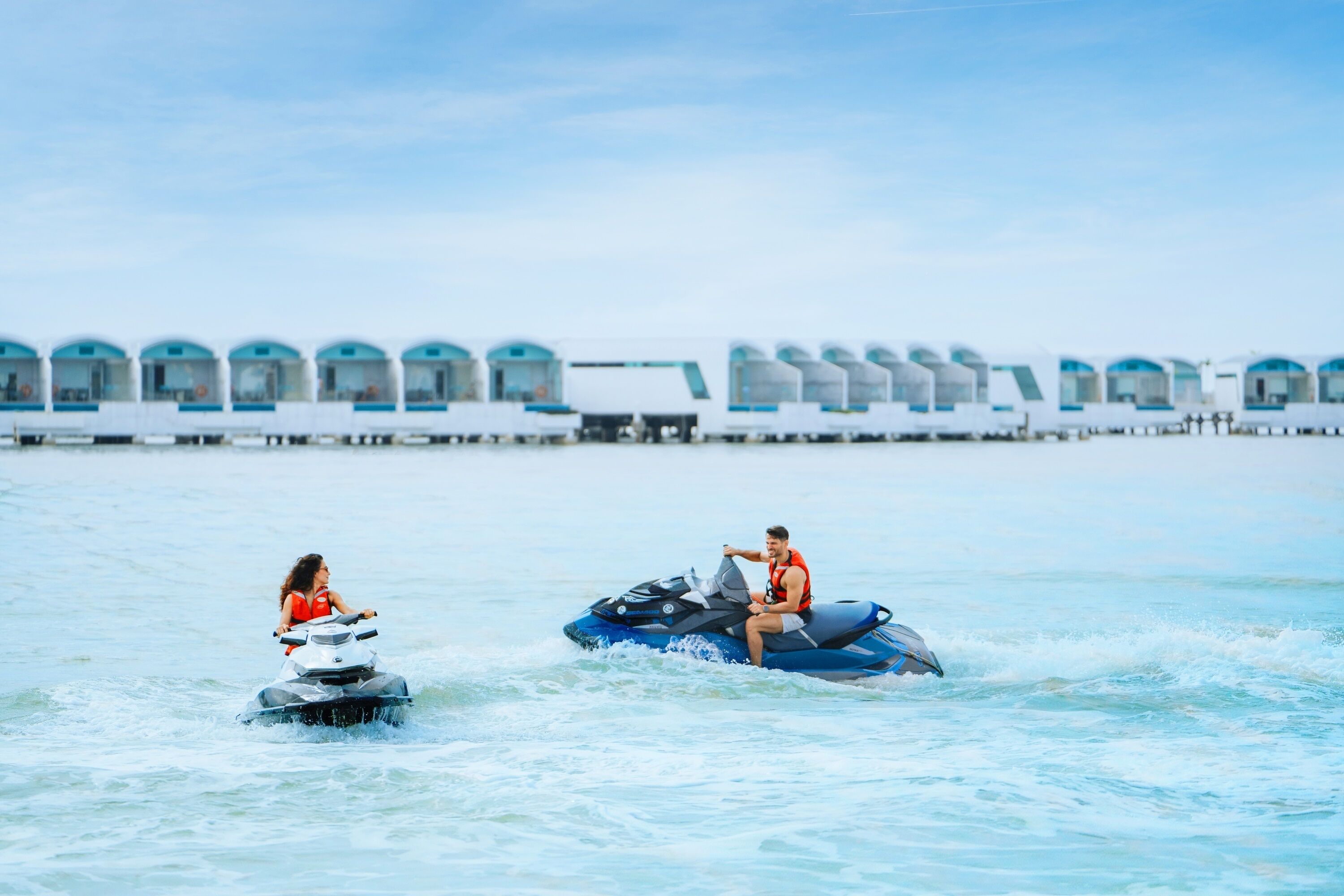 Un jet ski y un motorboat sobre aguas tranquilas, con una hilera de habitaciones de hotel al fondo.