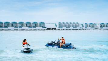 Un jet ski y un motorboat sobre aguas tranquilas, con una hilera de habitaciones de hotel al fondo.