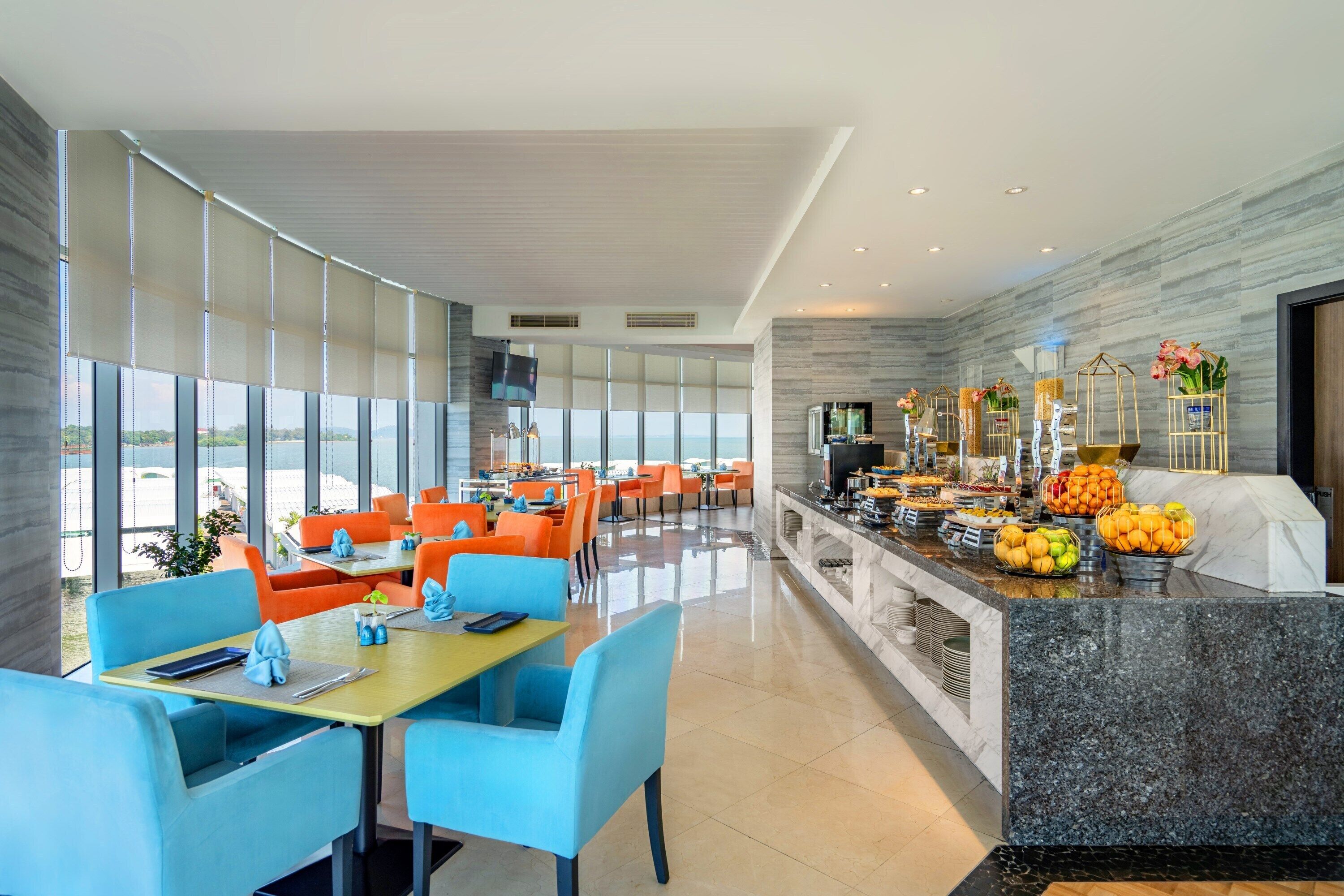 A modern restaurant with a buffet, bright orange chairs, and a view of the sea.