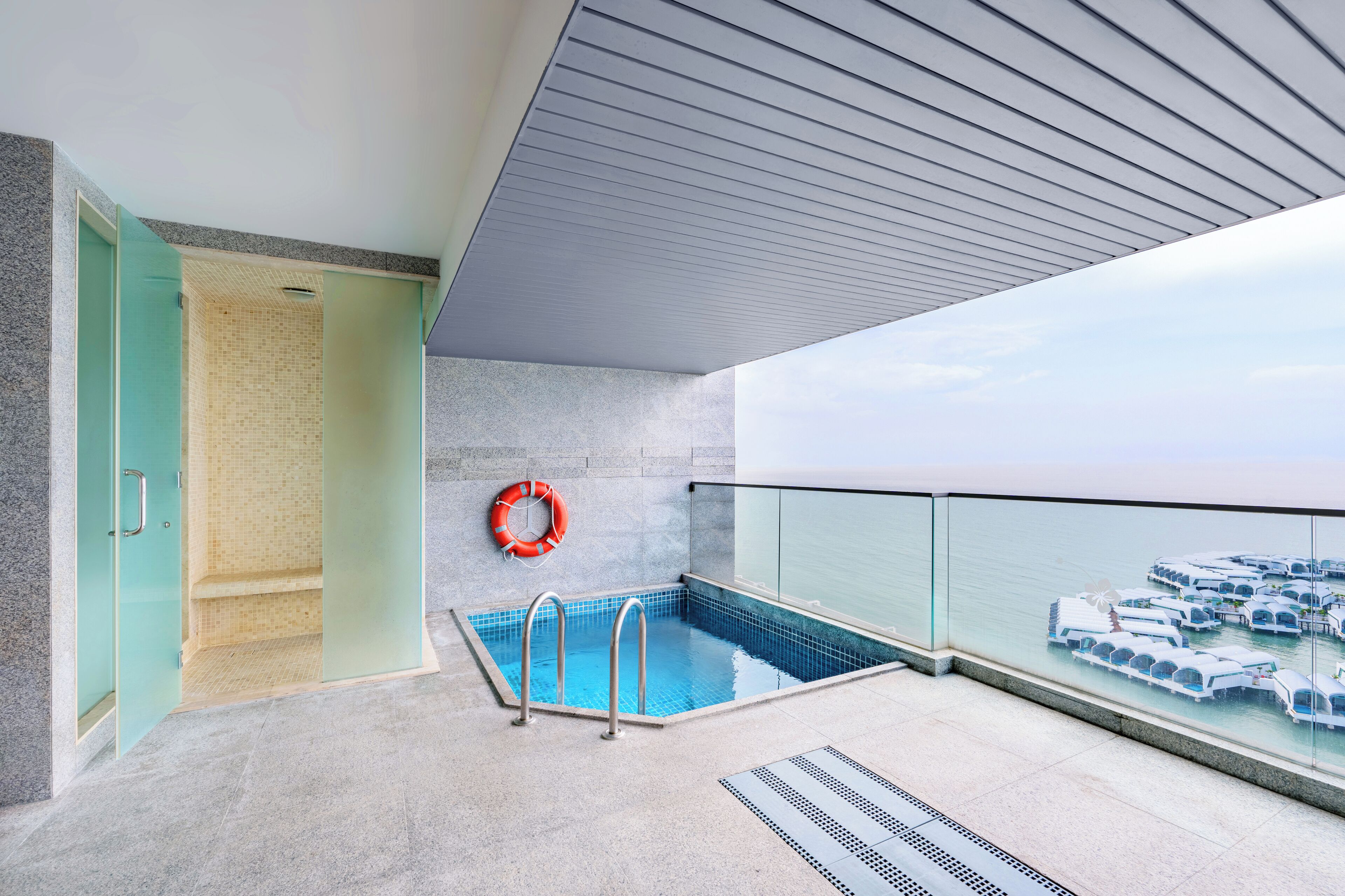 Un área de piscina interior moderna con paredes de vidrio transparente, suelo de baldosas y un flotador en la pared.