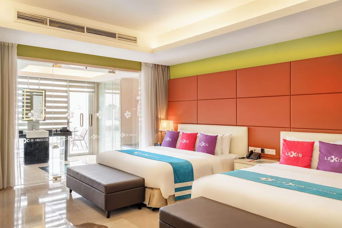 A hotel room with two beds, a sitting area, and a view of the hotel's lobby.