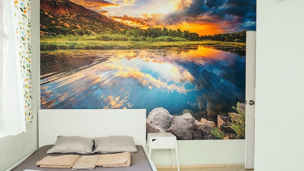 A bedroom with a bed, pillows, a bedside table, and a large landscape mural on the wall.