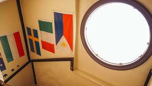 A staircase with handrails, a round window, and flags of Italy, Ireland, and the Philippines.