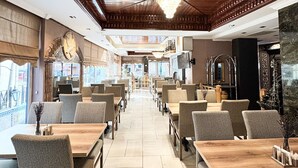 A restaurant with a long counter and multiple tables, a wooden ceiling, and a view of the street outside. - Ankara Royal Hotel (Ankara)