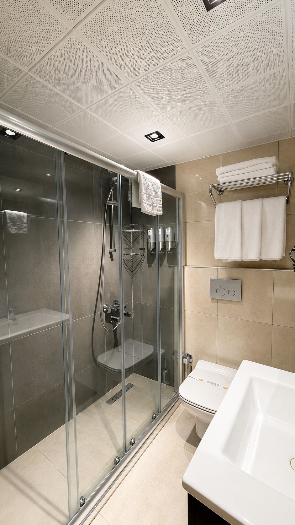 Un baño moderno con ducha envuelta en vidrio, un lavamanos blanco y un perchero para toallas.