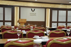 Une salle de conférence avec des tables disposées pour une réunion, des chaises rouges et dorées, un grand emblème sur le mur et un lustre.