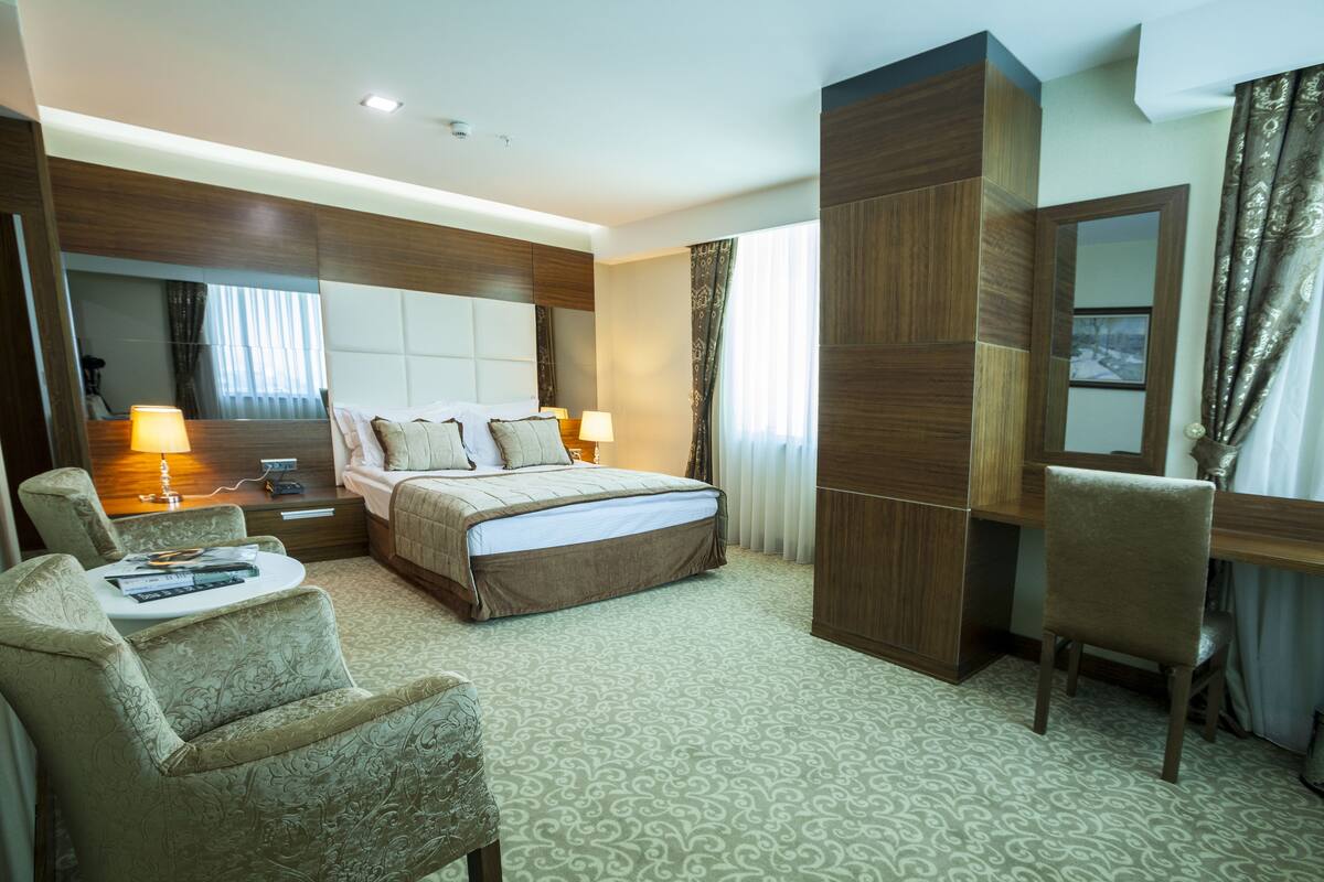 A hotel room with a large bed, a desk, a chair, a mirror, and a window with curtains.