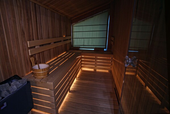 Un sauna en bois avec des bancs, un seau en bois et un récipient en pierre.