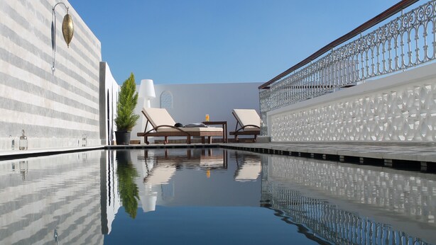 A pool area with two lounge chairs, a table, and a potted plant. - Riad Kalaa 2 (Rabat)