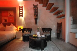 Una habitación acogedora con una cama, dos sillones, una mesita con un florero y una pared con un diseño geométrico.