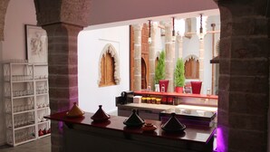 A kitchen with a wooden counter, shelves with glassware, and a red chair. - Riad Kalaa 2 (Rabat)