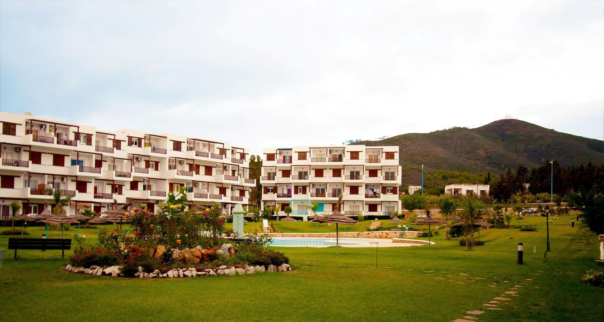 Un hotel de varios pisos con balcones, piscina y jardín ajardinado.
