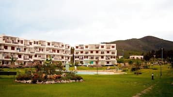 Un hotel de varios pisos con balcones, piscina y jardín ajardinado.