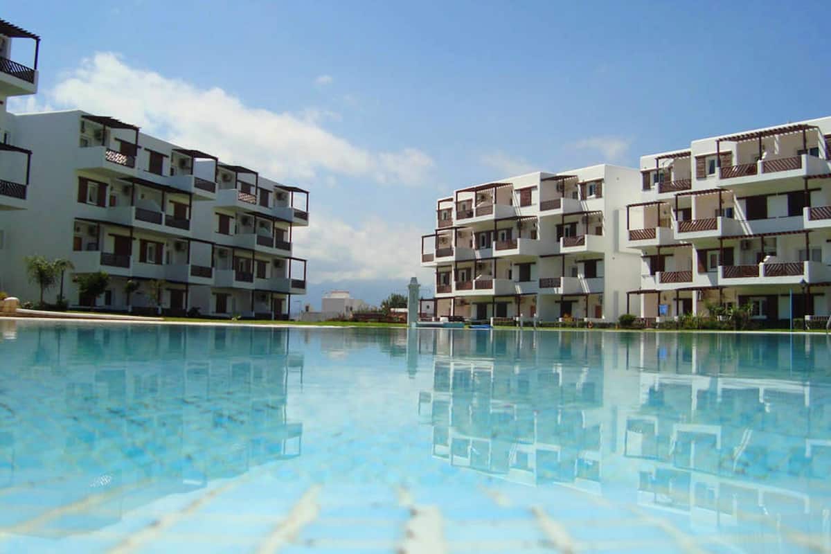Een modern hotel met meerdere balkons, een zwembad en een helderblauwe lucht.
