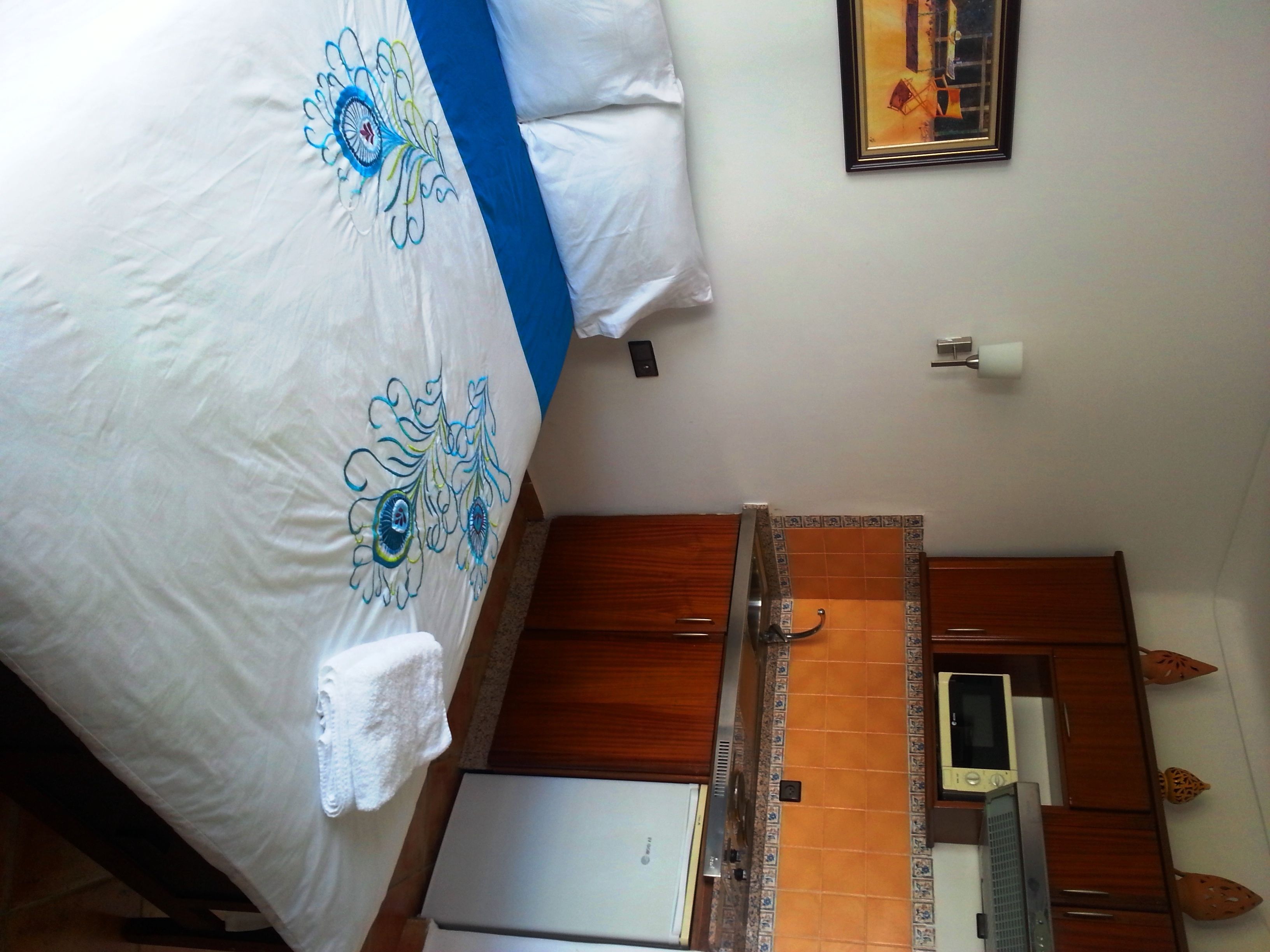 Quarto de hotel com uma cama, pequeno espaço de cozinha e banheiro.