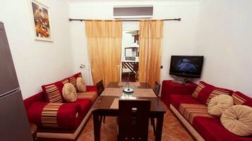 A compact living space with a dining table, two sofas, a TV, and a small kitchen area.