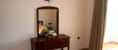 Quarto de hotel com uma cama, cômoda de madeira com espelho, um buquê de flores e uma televisão na parede.