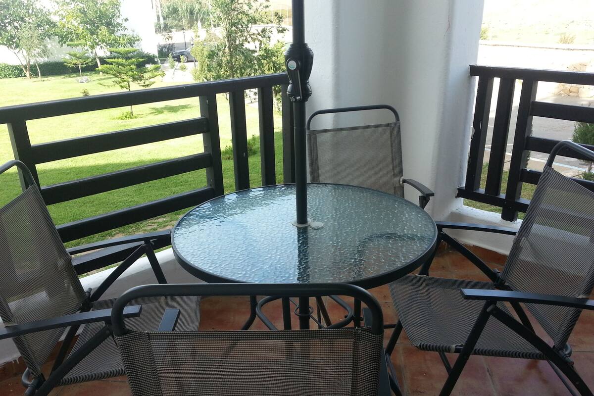 Een glazen ronde tafel met vier stoelen van netstof op een terras met een zwarte reling.