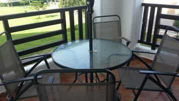 Een glazen ronde tafel met vier stoelen van netstof op een terras met een zwarte reling.