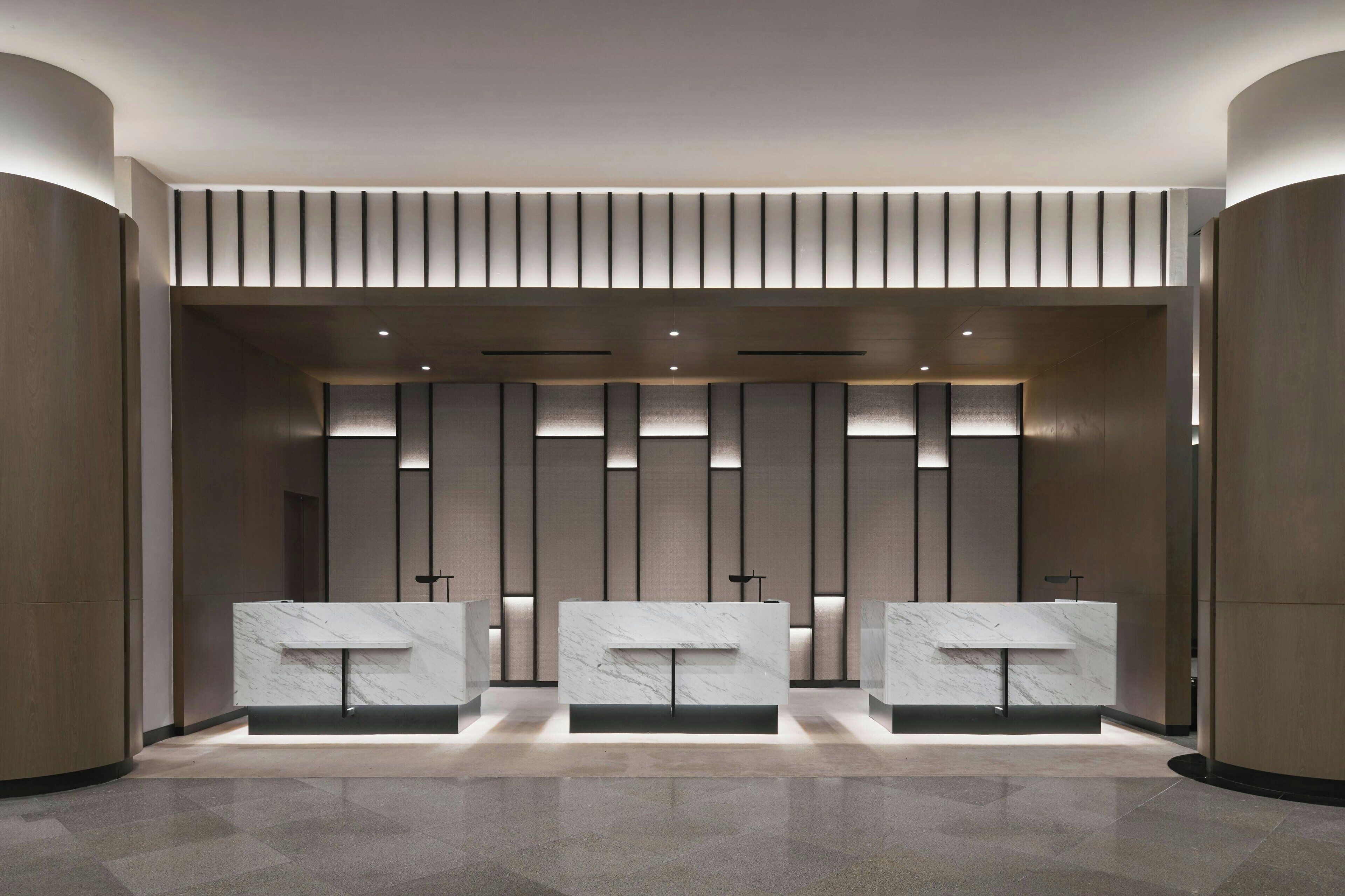 A modern reception area with three marble counters, vertical lighting panels, and a sleek, minimalist design.