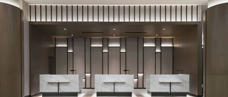 Un área de recepción moderna con tres mostradores de mármol, paneles de iluminación vertical y un diseño elegante y minimalista.