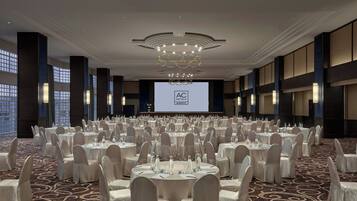 A large conference room with round tables, white chairs, and a large screen displaying "AC HOTELS MARBERT".