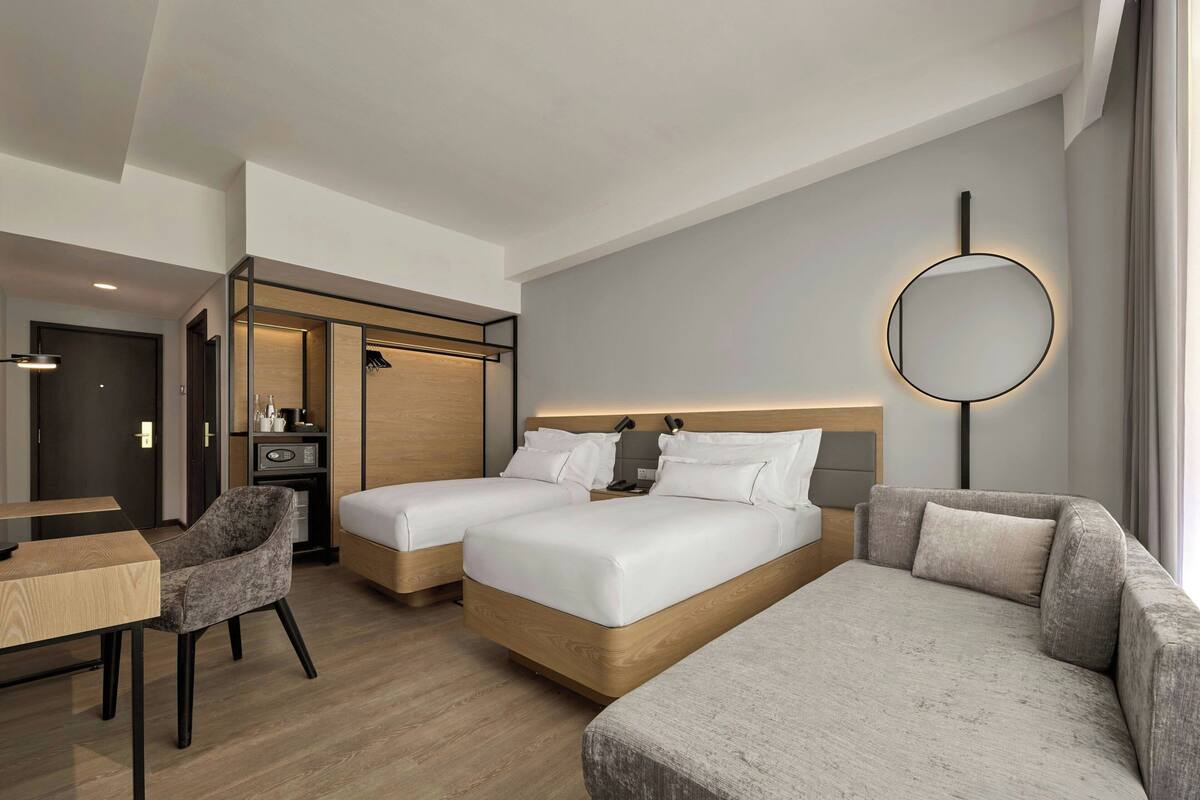 Ein Hotelzimmer mit zwei Betten, einer Schlafcouch, einem Schreibtisch und einem Kleiderschrank.
