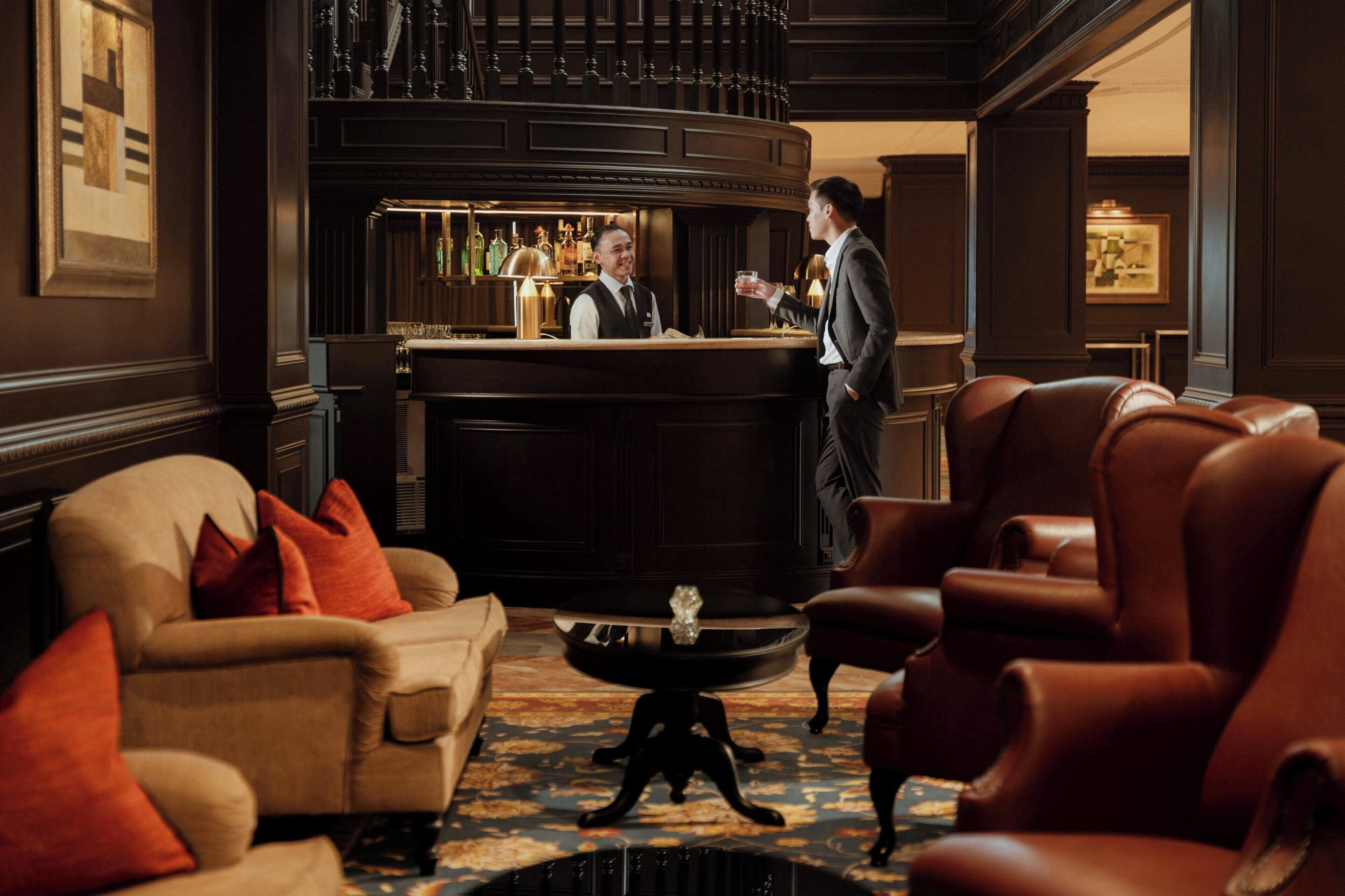 A bar area with leather chairs, a bar counter, and a bartender.