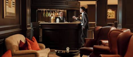 A bar area with leather chairs, a bar counter, and a bartender.