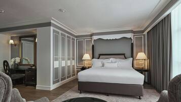 A spacious hotel room with a large bed, two bedside tables with lamps, a wardrobe, and a sitting area with a coffee table.