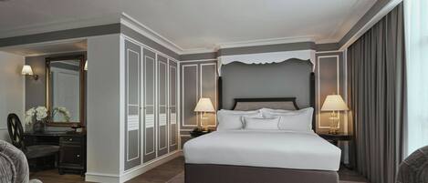 A spacious hotel room with a large bed, two bedside tables with lamps, a wardrobe, and a sitting area with a coffee table.