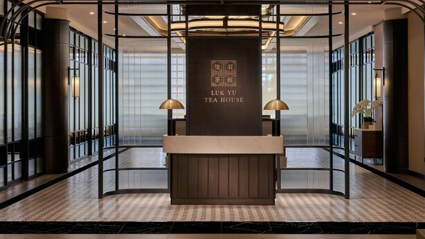 A reception area with a wooden counter, a sign reading "LUK YU TEA HOUSE," and a modern interior design with black and white patterned flooring.