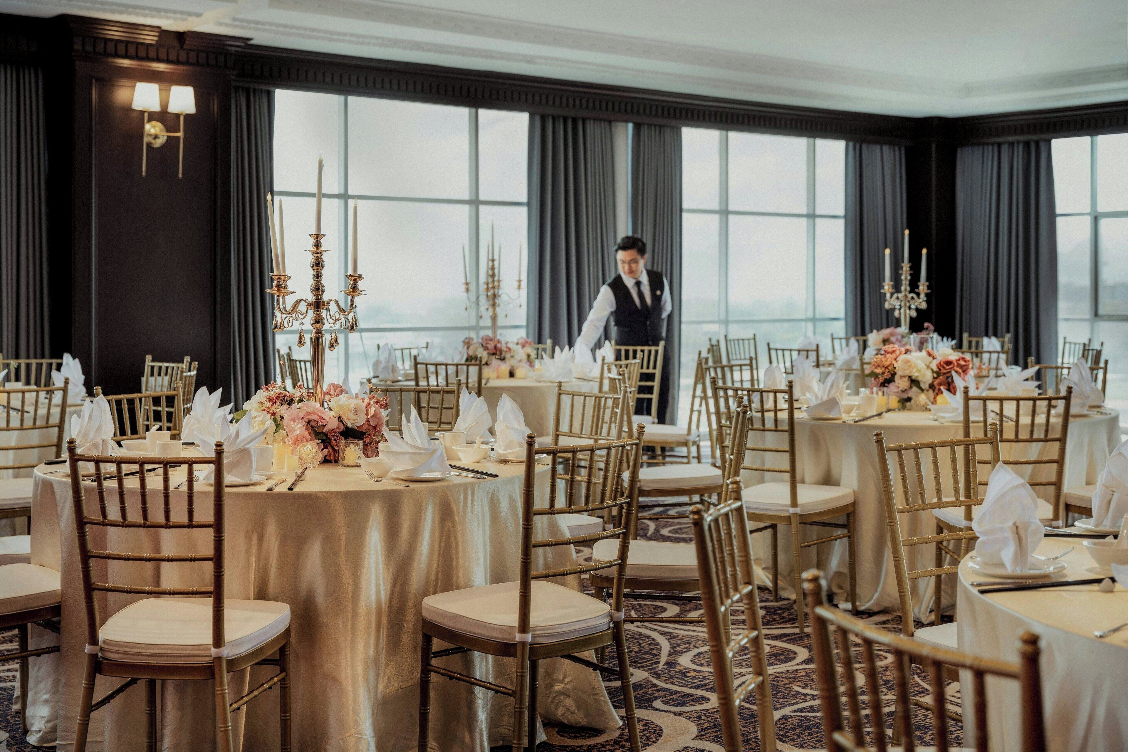 Ein Bankettsaal mit runden Tischen, goldenen Stühlen und floralen Tischdekorationen.