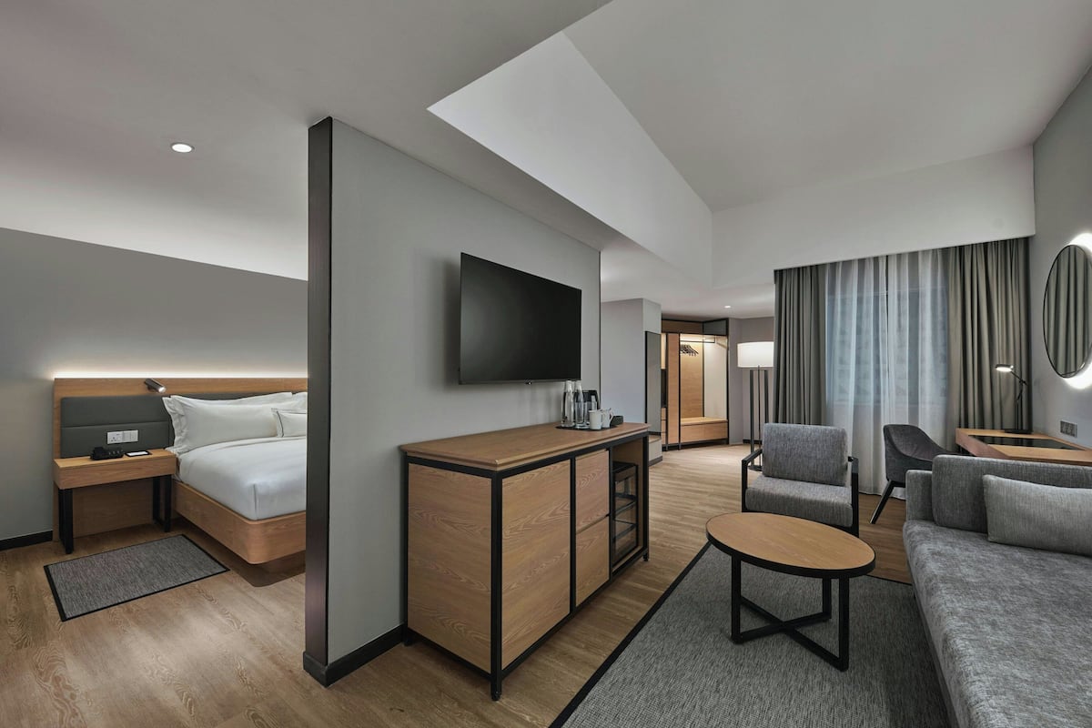 Ein modernes Hotelzimmer mit Bett, Schreibtisch, Fernseher, Sofa und Essbereich.