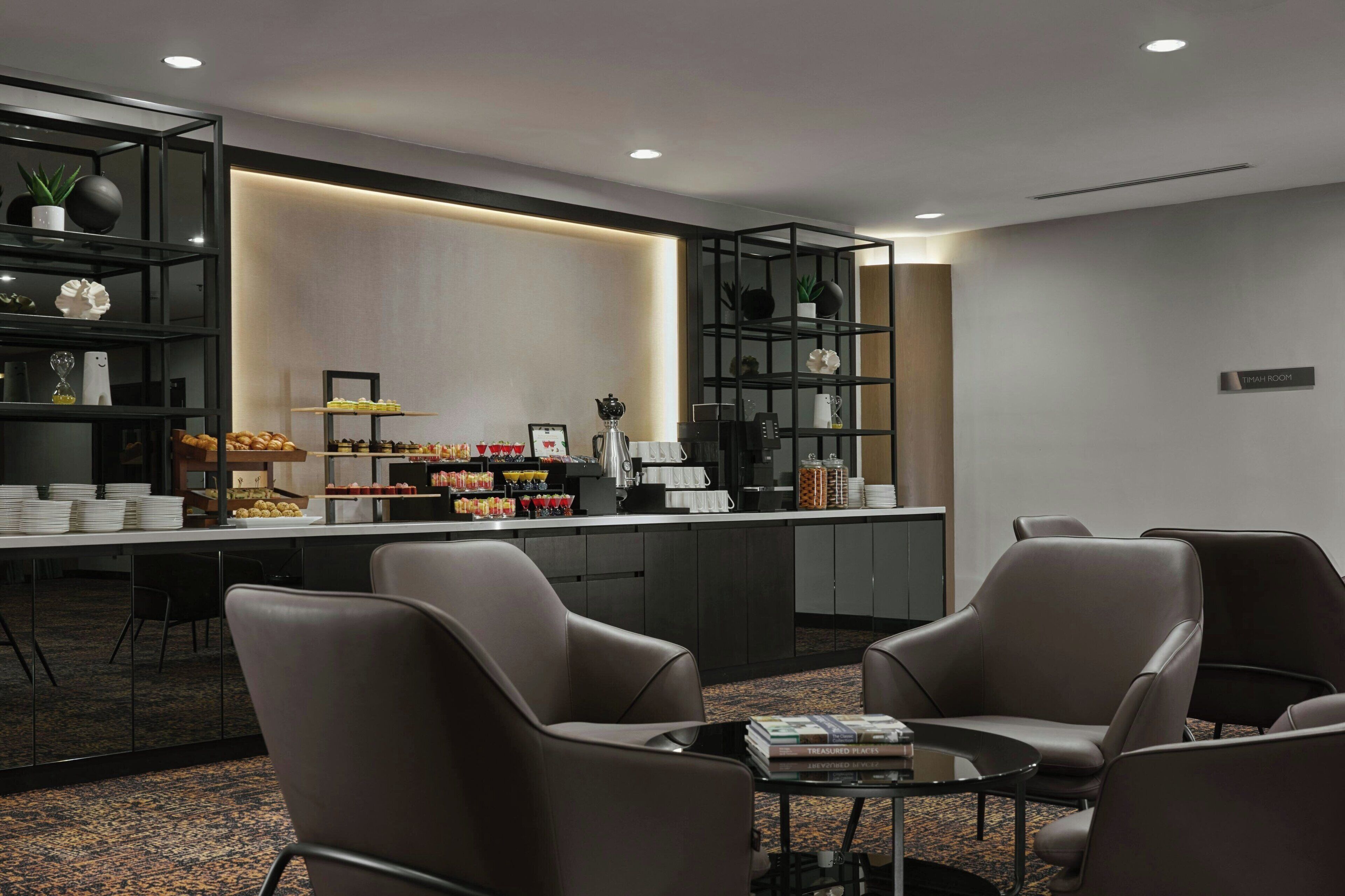 A modern hotel lobby with a reception desk, seating area, and shelves with amenities.