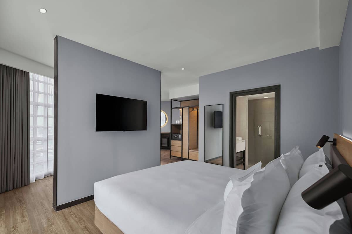 Ein modernes Hotelzimmer mit einem großen Bett, einem flachbildfernseher an der Wand und einem sichtbaren Badezimmer durch eine offene Tür.