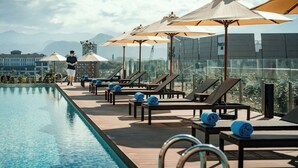 A rooftop pool area with lounge chairs and umbrellas, overlooking a cityscape.